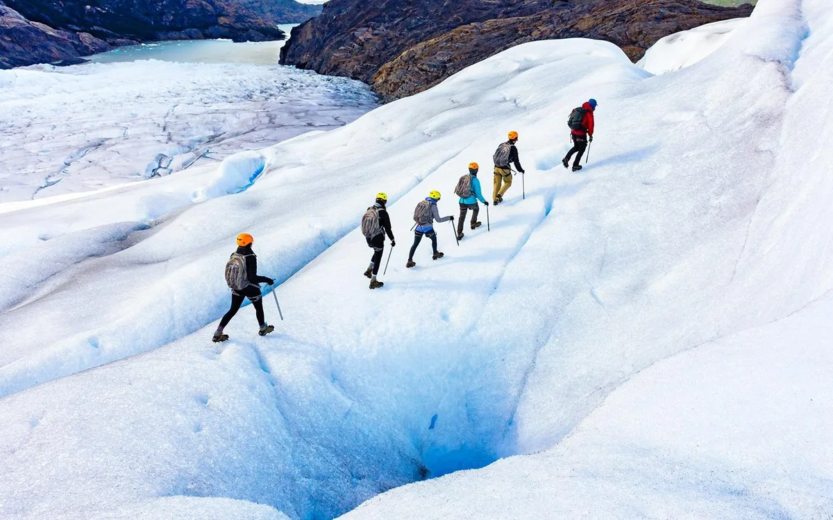 A roped line of walkers crossing a broken outlet glacier in helmets and crampons