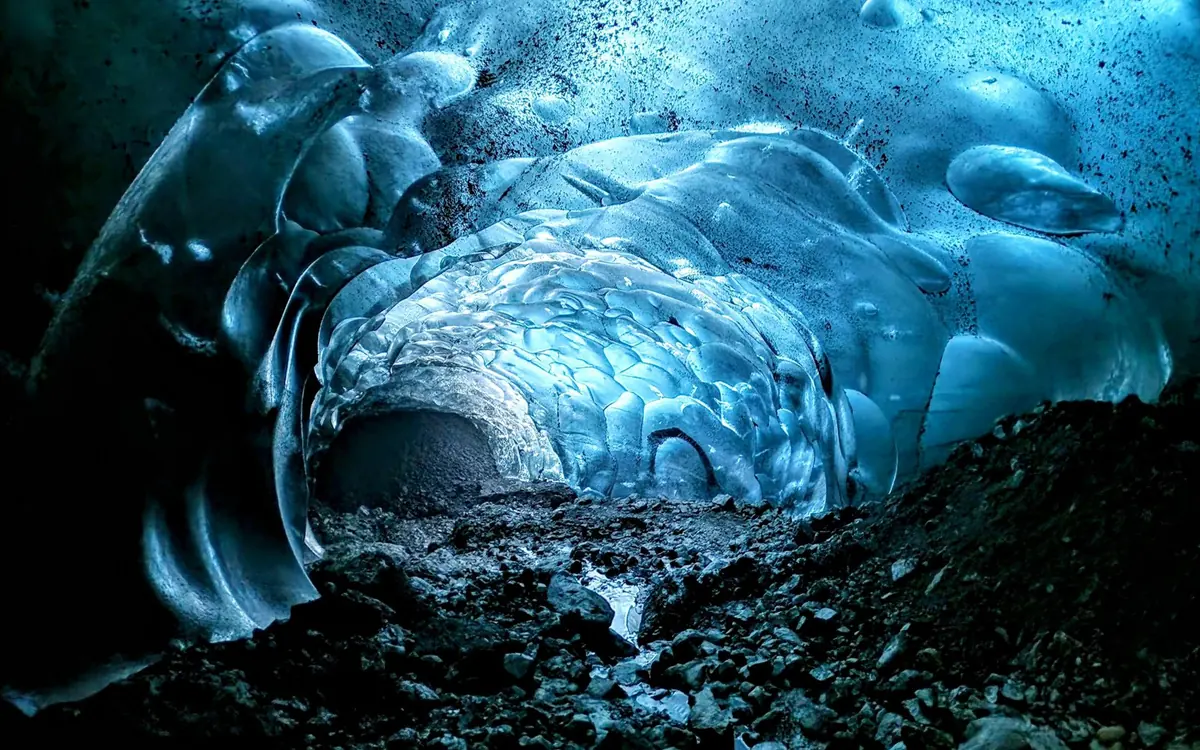 Die gewellte blaue Eisdecke einer natürlichen Höhle über einem Boden aus Fels und Schmelzwasser