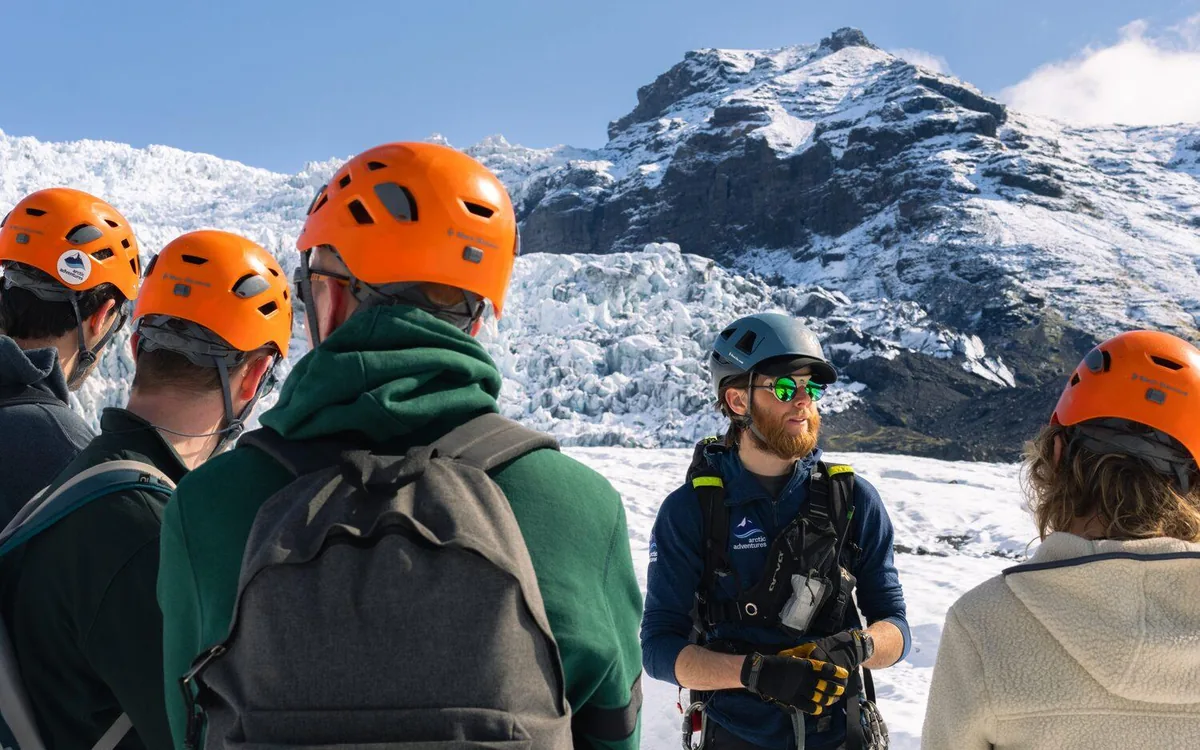 Grupa w kaskach i rakach stojąca na czole lodowca Falljökull z przewodnikiem