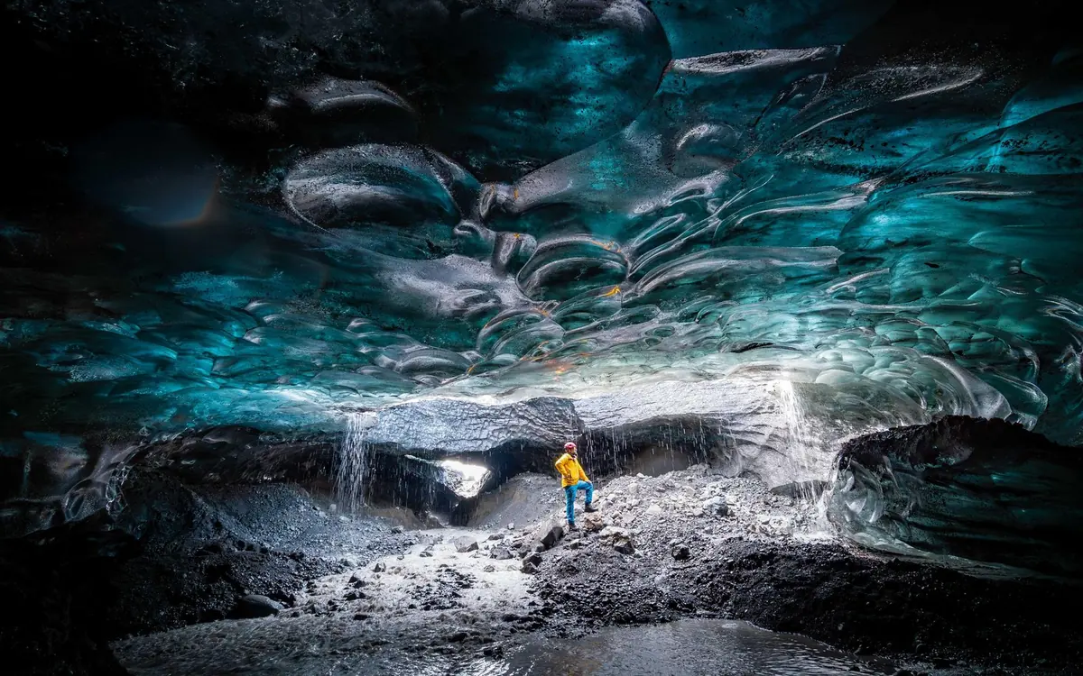 Ein Guide steht unter der blauen Decke einer Eishöhle, beleuchtet vom Tageslicht am Eingang
