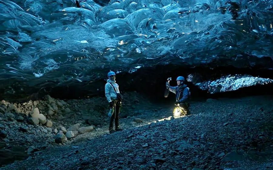 Zwei Wanderer mit Stirnlampen beleuchten die dunkle Eiswand einer Höhle