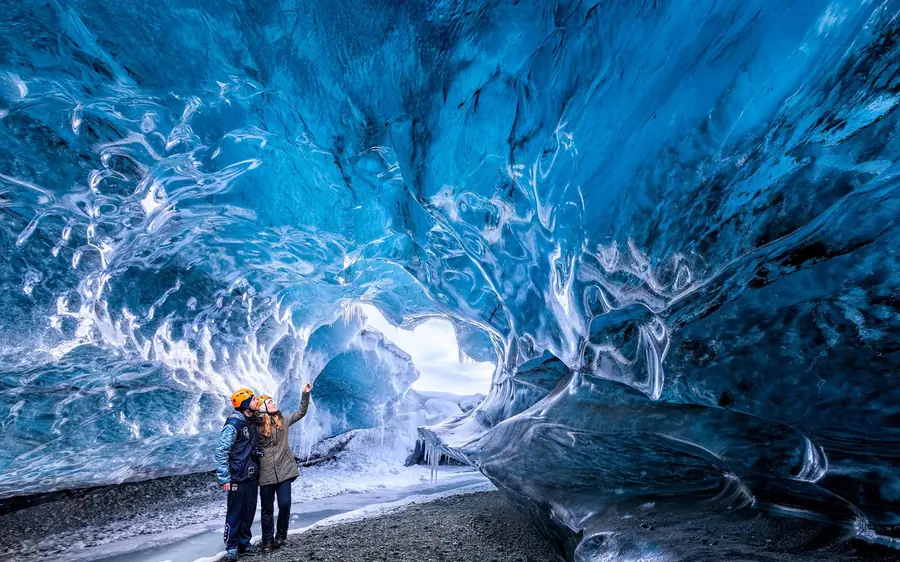 Ein Besucher in blauer Jacke unter dem weiten blauen Gewölbe einer Eishöhle