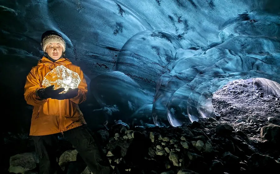 Ein Guide in gelber Jacke hält einen klaren Block Gletschereis in einer Höhle hoch