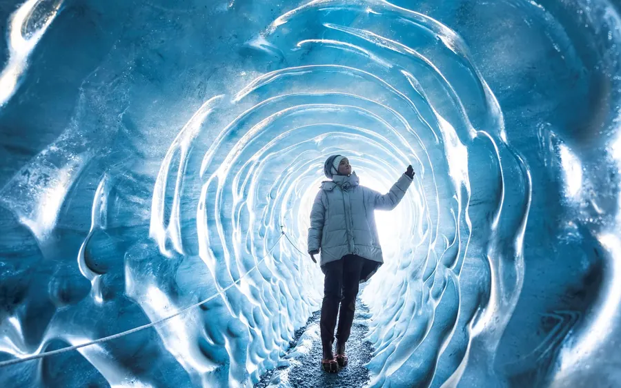 Ein Besucher geht in einen runden Tunnel aus geripptem blauem Eis
