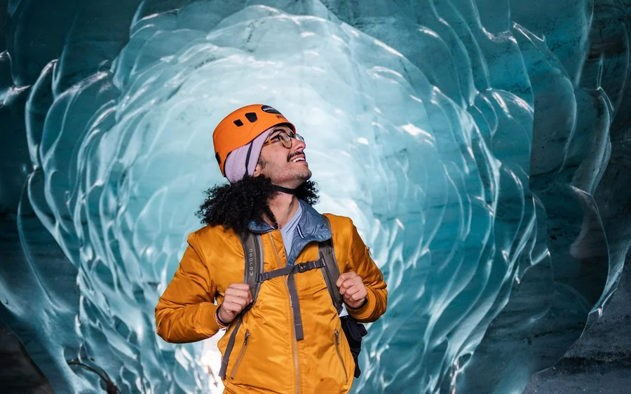 Ein Mann in orangefarbener Jacke und Helm steht in einer hellen Eishöhle