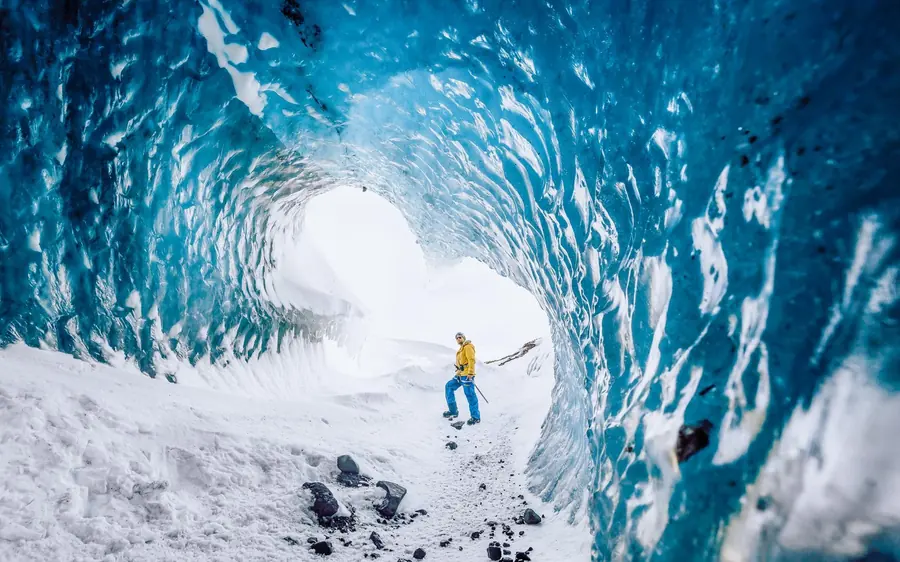 Eine einzelne Silhouette am hellen Eingang einer Eishöhle, Schmelzwasser läuft über den dunklen Boden
